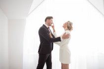 Jovem homem bonito em traje preto e mulher bonita em jaqueta branca em pé no quarto perto da janela e abraçando — Fotografia de Stock