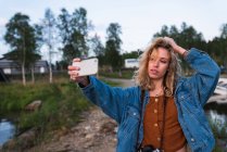 Young woman making selfie on coast of lake — Stock Photo