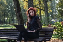 Женщина с ноутбуком и смартфоном на скамейке в парке — стоковое фото