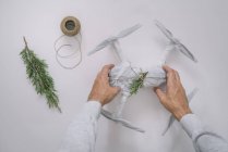 Чоловічі руки обгортають дрон як різдвяний подарунок з ялиновою гілкою та шпагатом на білому тлі — стокове фото