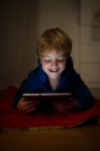 Fröhlicher kleiner Junge schaut Cartoons mit digitalem Tablet auf Holzboden — Stockfoto