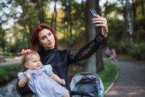 Mother taking selfie with cheerful baby girl in park — Stock Photo