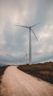 Fila de molinos de viento modernos de pie a un lado de la estrecha carretera rural en el día nublado - foto de stock