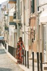 Елегантної жінки в довгій сукні, несучи сумочку і йшов по вулиці в сонячному світлі — стокове фото