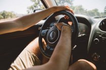 Невпізнаваний чоловік сидить на водійському сидінні і тримає руки на кермі під час подорожі по чудовій сільській місцевості на машині — стокове фото