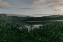 Чистое озеро, окруженное горами и зеленой травой на фоне неба с облаками — стоковое фото