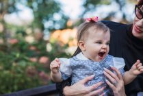 Femme tenant bébé rugissant drôle tout en étant assis sur le banc sur fond flou du parc — Photo de stock
