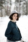 Досить молода жінка в стильному вбранні, дивлячись далеко, стоячи біля дерева, вкритого снігом в холодний день в чудовій сільській місцевості — стокове фото