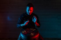 Young percussionist practicing technique with the tam tam or drum, colored lighting in red and blue. — Stock Photo
