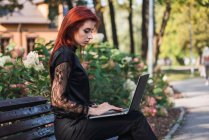 Elegante giovane donna che utilizza il computer portatile sulla panchina nel parco — Foto stock