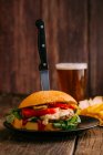 Delizioso hamburger gourmet con coltello su piatto su sfondo di legno scuro con birra e patatine fritte — Foto stock