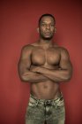 Fiducioso uomo afroamericano senza camicia in denim in piedi con le braccia incrociate guardando la fotocamera su sfondo rosso — Foto stock