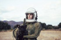 Дівчина в старому космічному шоломі тримає собаку в природі — стокове фото