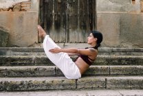 Barfüßige Frau in Bootspose beim Yoga auf verwitterten Stufen eines antiken Gebäudes — Stockfoto