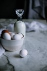 Миска з курячих яєць і пляшка свіжого молока, що стоїть на мармуровій стільниці на кухні — стокове фото