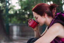 Young sportswoman sitting outdoors and drinking coffee — Stock Photo