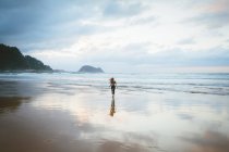 Back view of young woman standing on wet sand of beach near waving sea on cloudy day in Zarautz, Spain — Stock Photo