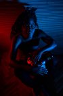 Jeune homme rastafari africain aime répéter et joue udu, éclairage coloré rouge et bleu — Photo de stock