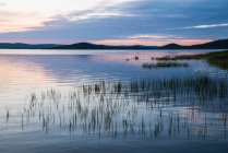 Superficie de tranquilo lago azul con cielo nublado al atardecer, Laponia - foto de stock