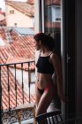 Young woman in lingerie standing at balcony with view of old roofs — Stock Photo