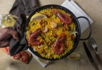 Human hand holding pan of traditional spanish paella marinera with rice, prawns, squid and mussels — Stock Photo