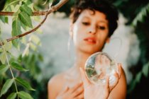 Young topless brunette covering breast and holding glass transparent ball in green woods — Stock Photo