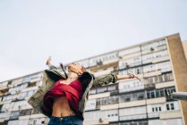 Excited young woman with arms outstretched standing against residential building — Stock Photo