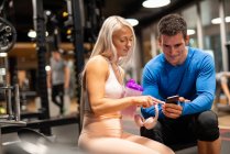 Athletic man and woman using smartphone in gym — Stock Photo