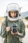 Girl wearing old space helmet and spacesuit holding photo camera outdoors — Stock Photo