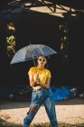 Encantadora joven con un traje elegante que sostiene el paraguas transparente mientras está de pie en la calle en el día soleado - foto de stock