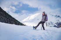 Side view of female in warm clothes lifting leg with ski while standing on snowy mountain slope — Stock Photo