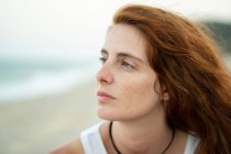 Mulher bonita com cabelo de gengibre olhando para longe enquanto estava de pé no fundo borrado de praia e mar em Tyulenovo, Bulgária — Fotografia de Stock