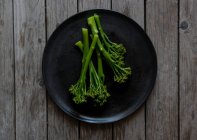 Brócolis cozido no vapor na placa preta na mesa de madeira — Fotografia de Stock