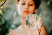 Giovane bruna in topless che tiene in mano una palla di vetro trasparente in boschi verdi — Foto stock