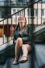 Laughing red-haired girl with braids sitting on stairs in city — Stock Photo