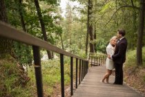 From above shot of embracing adult bride and groom standing on wooden walkway in green woods — Stock Photo