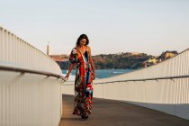 Элегантная женщина в длинном платье прогулка по мосту в летнем городе — стоковое фото