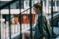 Pensive red-haired girl with braids sitting on staircase in city — Stock Photo