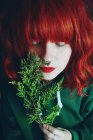 Young red haired woman holding fir twig in front of face — Stock Photo