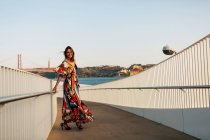 Elegante donna in abito lungo passeggiando sul ponte in città estiva — Foto stock