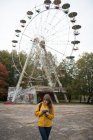 Rückansicht einer blonden Frau mit Kamera, die ein Foto von einem verlassenen Freizeitpark mit Attraktionen macht — Stockfoto