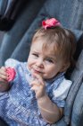Lovely baby girl looking at camera and eating sweet cookie while sitting in comfortable carriage — Stock Photo