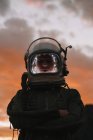 Chica con casco espacial viejo y traje espacial contra el cielo dramático al atardecer - foto de stock