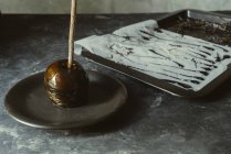 Schwarzer Karamell-Apfel am Stiel auf Teller auf grauer Tischplatte — Stockfoto