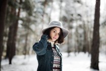 Jolie jeune femme en tenue élégante regardant loin tout en se tenant près d'un arbre couvert de neige par temps froid dans une magnifique campagne — Photo de stock