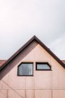 Dos ventanas de forma inusual en la pared bajo el techo de la casa de campo contra el cielo nublado - foto de stock