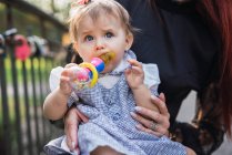 Baby girl sitting on mother lap with toy in park — Stock Photo