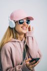 Mulher elegante com capuz rosa e boné ouvindo música com fones de ouvido — Fotografia de Stock