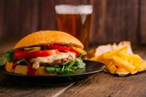 Köstlicher Gourmet-Burger auf Teller auf dunklem Holzgrund mit Bier und Pommes — Stockfoto