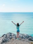 Woman in shorts standing on edge of cliff above endless blue sea water — Stock Photo